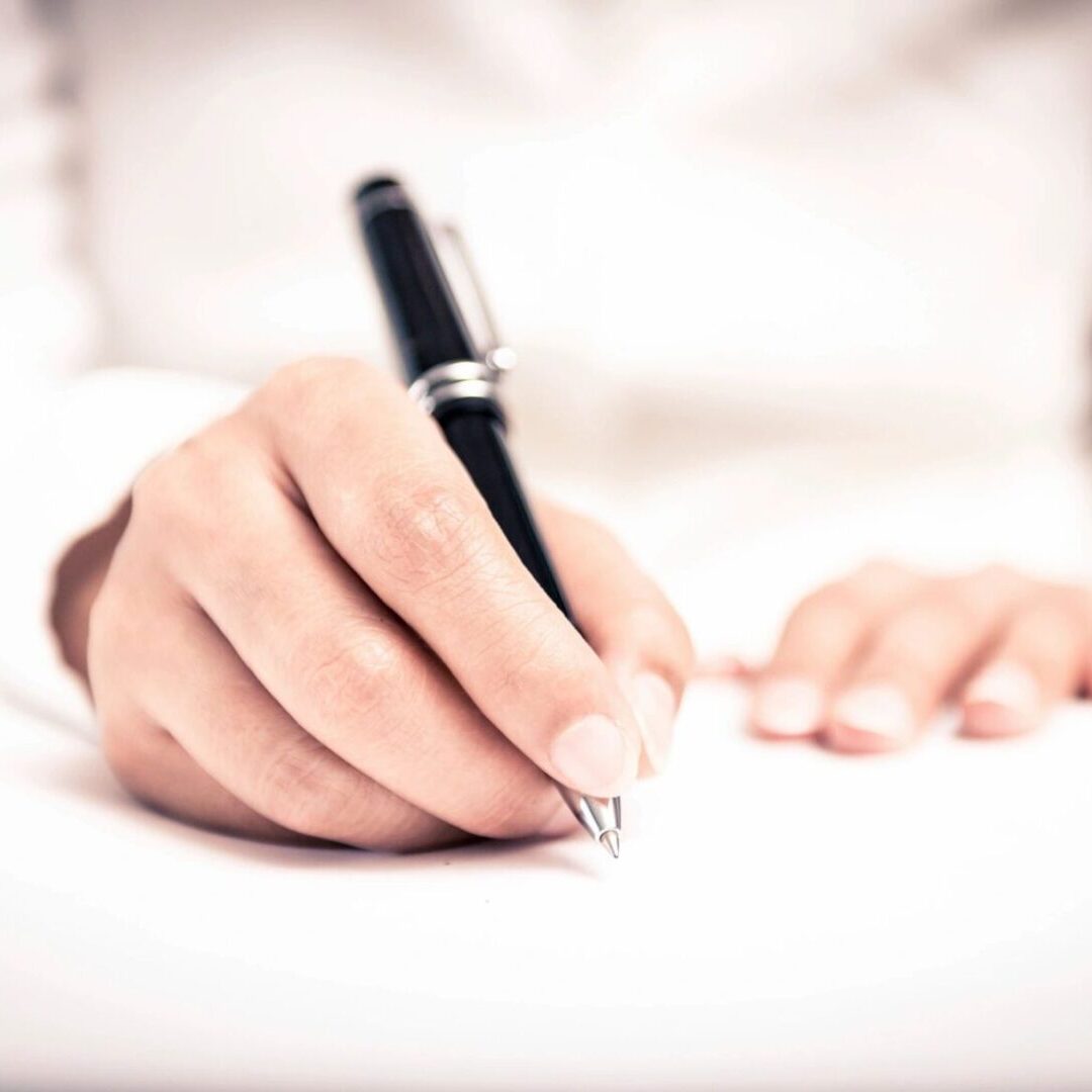 A person writing on paper with a pen.