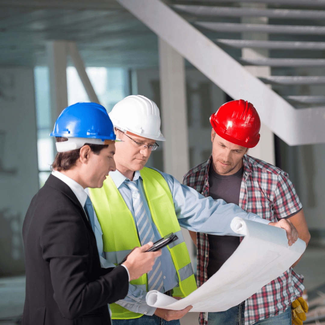 Three men in hard hats and vests looking at a plan.